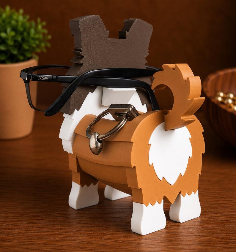 May include: A wooden dog-shaped eyeglasses holder in brown, white, and tan. The dog has a tail and is wearing black eyeglasses. The holder has a metal ring attached to the dog's body. The dog is sitting on a wooden surface.