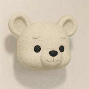 May include: A cream-colored bear head with black eyes and nose. The bear has rounded ears and a textured surface. The design is simple and cartoonish, with a smiling expression. The bear is a decorative item.