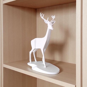 May include: A white deer ornament with detailed antlers stands on a wooden shelf. The deer is a minimalist design, with a smooth finish. The figurine is a decorative accent for home decor.