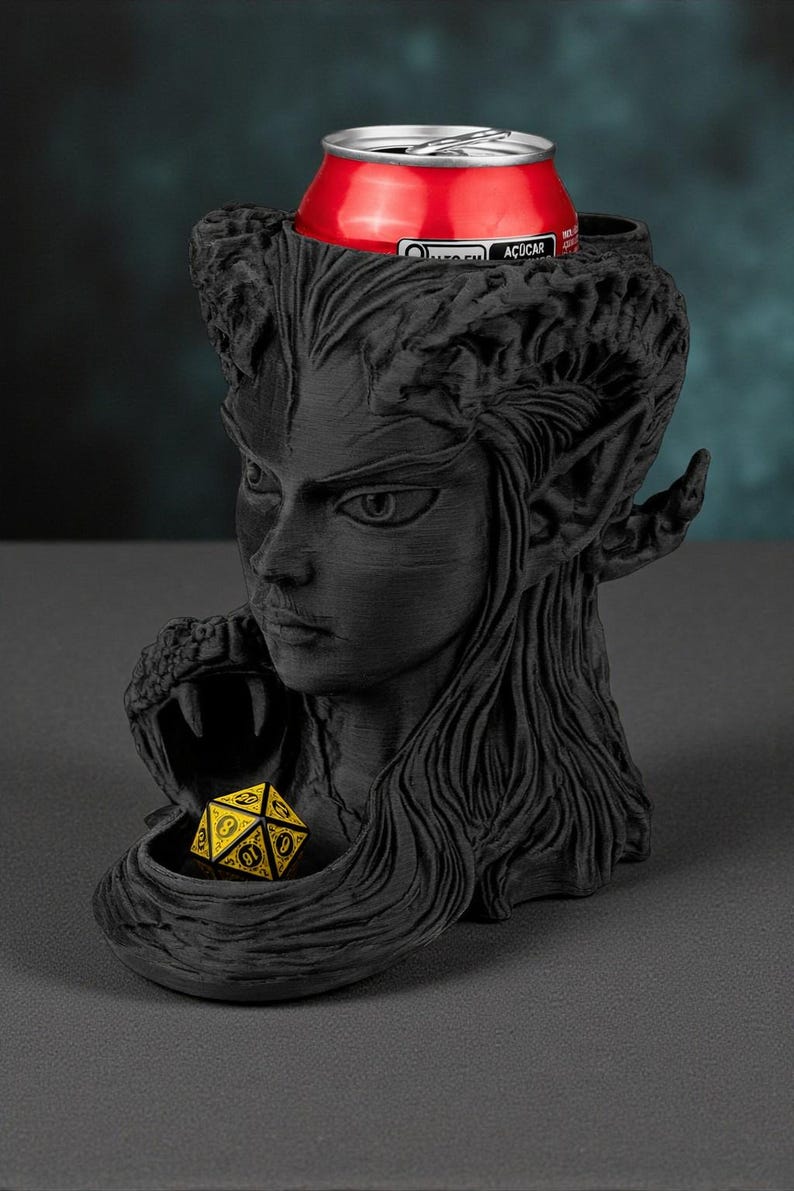 May include: A black, 3D-printed fantasy-themed drink holder featuring a woman's face with long hair and pointed ears. A red can sits in the holder's top, and a yellow and black die rests in a lower compartment. The holder is designed for tabletop gaming.