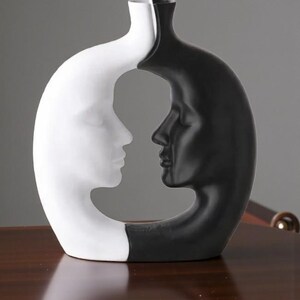 K&ouml;nnte beinhalten: Eine dekorative Vase in einem einzigartigen Design, das zwei Gesichter im Profil zeigt, eines wei&szlig; und eines schwarz. Die Vase hat eine glatte Oberfl&auml;che und eine moderne &Auml;sthetik, geeignet f&uuml;r die Inneneinrichtung.