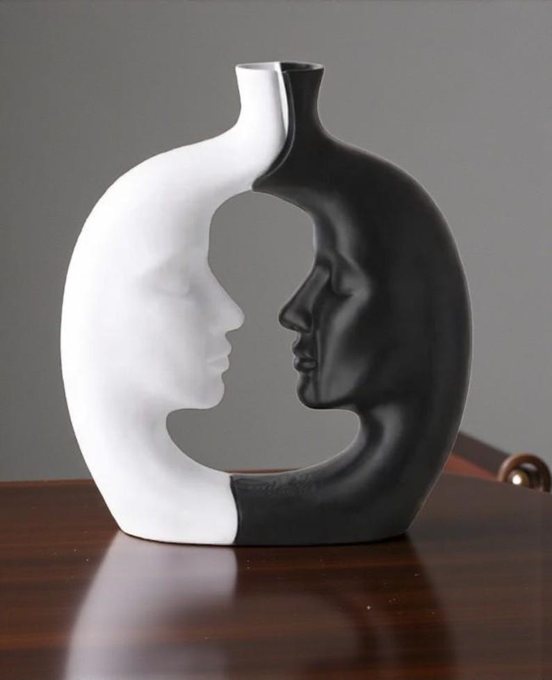 K&ouml;nnte beinhalten: Eine dekorative Vase in einem einzigartigen Design, das zwei Gesichter im Profil zeigt, eines wei&szlig; und eines schwarz. Die Vase hat eine glatte Oberfl&auml;che und eine moderne &Auml;sthetik, geeignet f&uuml;r die Inneneinrichtung.