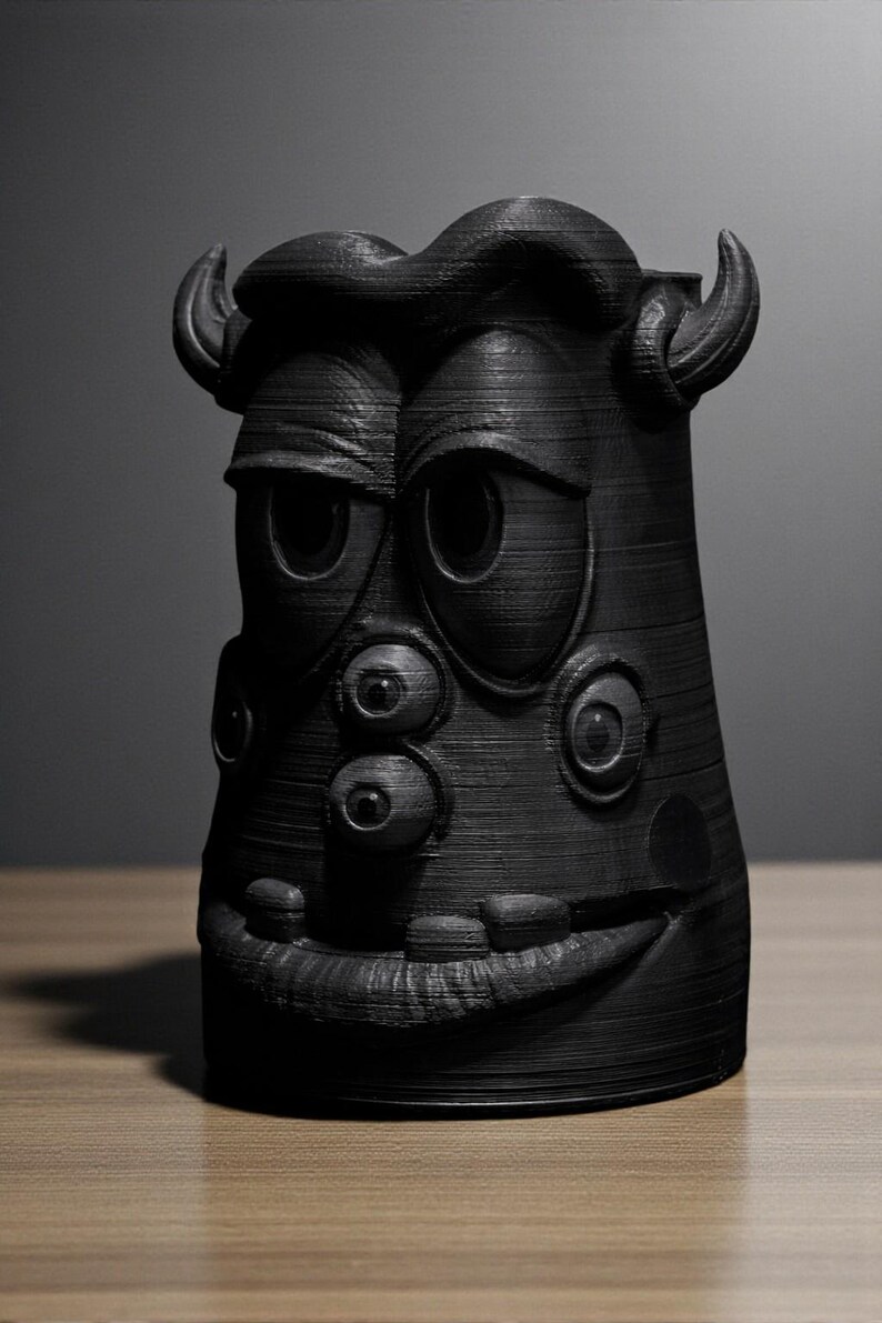 May include: A black, 3D-printed monster-like sculpture with multiple eyes, horns, and a wide grin. The textured surface and cartoonish design give it a whimsical appearance. The sculpture is likely a decorative item or a unique piece of art.