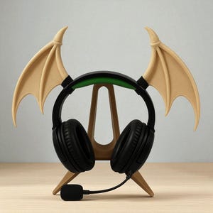 May include: Black headphones with a green and black headband, resting on a wooden stand. The stand is shaped like a stylized A-frame and features two tan-colored, bat-like wings attached to the headphones.