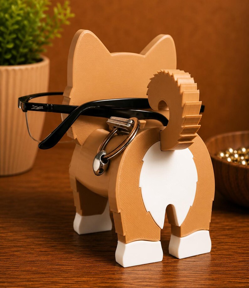 May include: A wooden corgi-shaped glasses holder in shades of brown and white, with black-framed glasses resting on it. The holder features a safety pin detail and a fluffy tail. The design is whimsical and functional, perfect for desk organization.