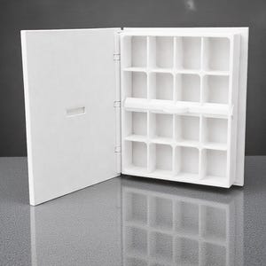 Peut inclure: Un organisateur blanc ouvert pour bijoux ou petits objets, avec de multiples compartiments carr&eacute;s. L'organisateur a une porte &agrave; charni&egrave;re &agrave; gauche et se refl&egrave;te sur une surface grise brillante. L'int&eacute;rieur est divis&eacute; en petits espaces de rangement individuels.
