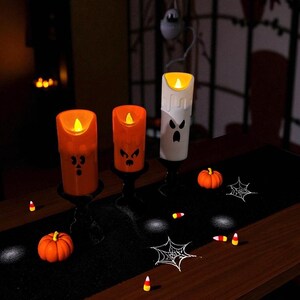May include: Halloween-themed decor featuring three illuminated candle-shaped lights with carved faces. Two are orange, one is white. The scene includes small pumpkins, spiderwebs, and candy corn on a black runner, creating a festive atmosphere.