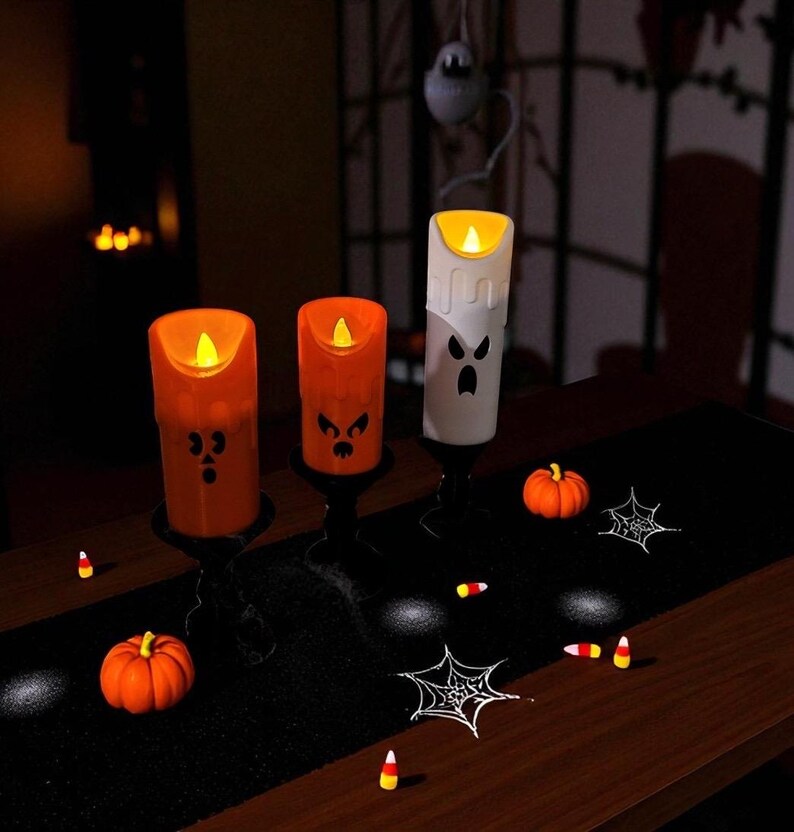 May include: Halloween-themed decor featuring three illuminated candle-shaped lights with carved faces. Two are orange, one is white. The scene includes small pumpkins, spiderwebs, and candy corn on a black runner, creating a festive atmosphere.