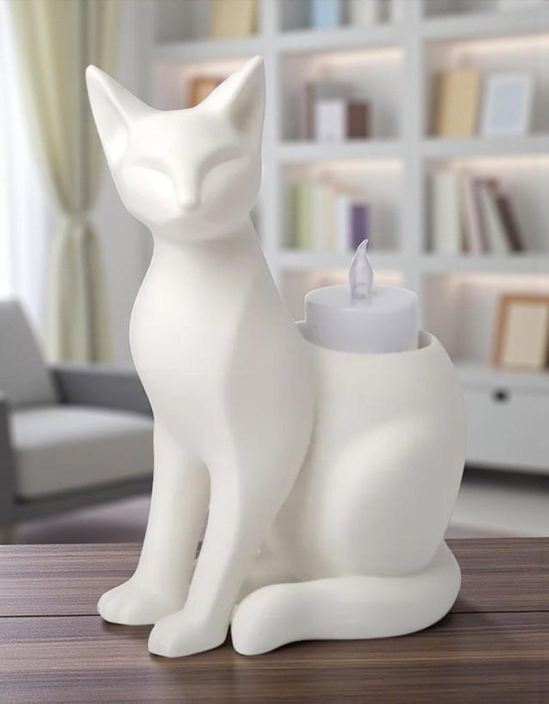 Op de afbeelding: Een witte keramische kattenfiguur met een kaarsenhouder. De kat zit rechtop met gesloten ogen. Een witte LED-kaars zit in de houder. De figuur staat op een houten oppervlak.