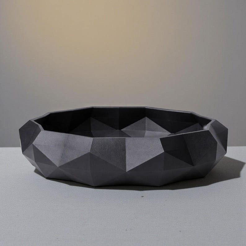 K&ouml;nnte beinhalten: Eine dunkelgraue, geometrische Schale mit facettiertem Design. Die Schale hat ein niedriges Profil und eine breite &Ouml;ffnung. Die Oberfl&auml;che ist matt und die Schale ist wahrscheinlich aus einem festen Material gefertigt. Geeignet f&uuml;r dekorative oder funktionale Zwecke.