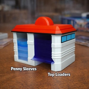 Puede incluir: Una caja de almacenamiento de tarjetas blanca y roja con detalles en azul. La caja tiene un techo rojo y una peque&ntilde;a estructura roja redondeada en la parte superior. El texto "Penny Sleeves" y "Top Loaders" est&aacute; impreso en la parte delantera.