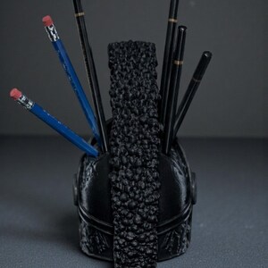 Puede incluir: Organizador de escritorio negro con una parte delantera decorativa texturizada y un divisor central texturizado. Los l&aacute;pices de varios colores se colocan dentro del organizador, incluidos l&aacute;pices azules con gomas rosas y l&aacute;pices negros.