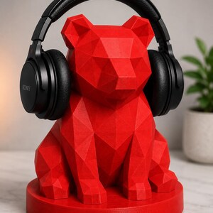 Puede incluir: Un soporte para auriculares con forma de oso geom&eacute;trico rojo que sostiene auriculares negros. El soporte est&aacute; hecho de una serie de formas triangulares y se asienta sobre una base redonda. Los auriculares tienen auriculares negros y una diadema negra. La marca "SONY" es visible.