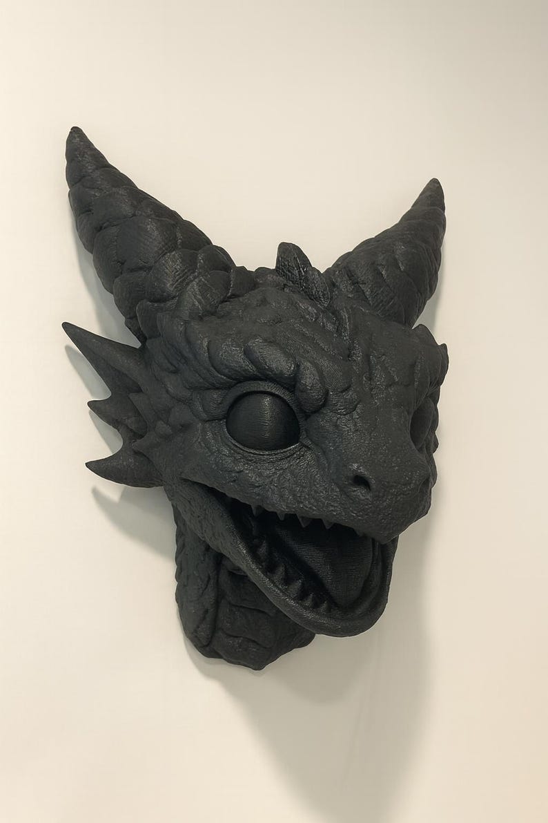 May include: A black dragon head sculpture with textured details, including horns, scales, and an open mouth revealing teeth. The dragon head is mounted on a white wall, showcasing a detailed fantasy art piece.