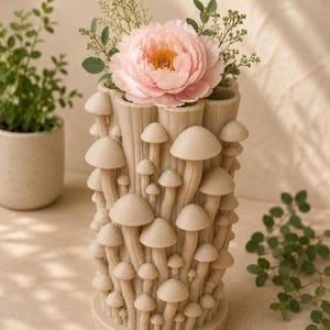 K&ouml;nnte beinhalten: Eine beige Vase mit Pilz-Motiv h&auml;lt eine gro&szlig;e rosa Pfingstrose und Gr&uuml;nzeug. Die zylindrische Vase hat eine strukturierte Oberfl&auml;che und ist mit Pilzformen in verschiedenen Gr&ouml;&szlig;en bedeckt. Die Gesamt&auml;sthetik ist skurril und von der Natur inspiriert.