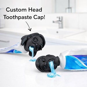 May include: Two black custom head toothpaste caps are attached to toothpaste tubes, dispensing blue toothpaste. The caps are designed to look like a face. The text "Custom Head Toothpaste Cap!" is at the top of the image.