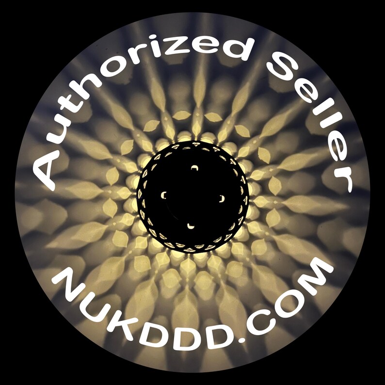 May include: Circular image with a black center and a decorative pattern of light and shadow. The words "Authorized Seller" and "NUKDDD.COM" are written in white around the edge of the circle.