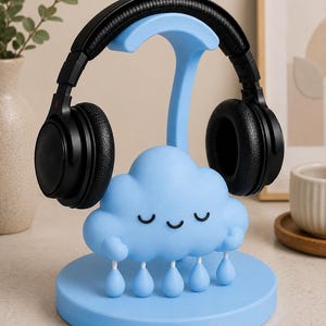 May include: A light blue headphone stand shaped like a cloud with raindrops, holding a pair of black headphones. The stand has a round base and a curved support for the headphones. The cloud has closed eyes.