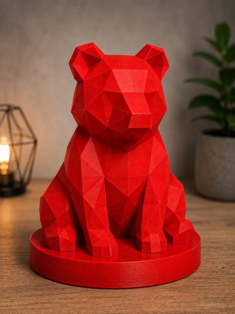 Puede incluir: Una vibrante escultura de oso geom&eacute;trico rojo. El oso est&aacute; sentado erguido sobre una base circular. La superficie de la escultura est&aacute; compuesta por numerosos planos planos, creando una apariencia facetada. El oso es una pieza decorativa s&oacute;lida y llamativa.