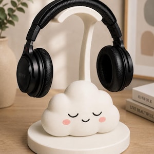 K&ouml;nnte beinhalten: Schwarzer Sony Over-Ear-Kopfh&ouml;rer auf einem wei&szlig;en Kopfh&ouml;rerst&auml;nder in Wolkenform. Die Wolke hat ein l&auml;chelndes Gesicht mit rosa Wangen. Der St&auml;nder steht auf einer wei&szlig;en kreisf&ouml;rmigen Basis. Die Kopfh&ouml;rer sind schwarz.