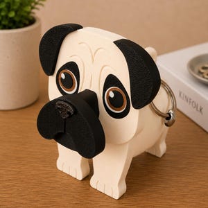 May include: A cream-colored pug figurine with black ears, nose, and accents. The dog-shaped item has large brown eyes and a metal ring attached to its side. The pug is standing on four legs and is a decorative item.