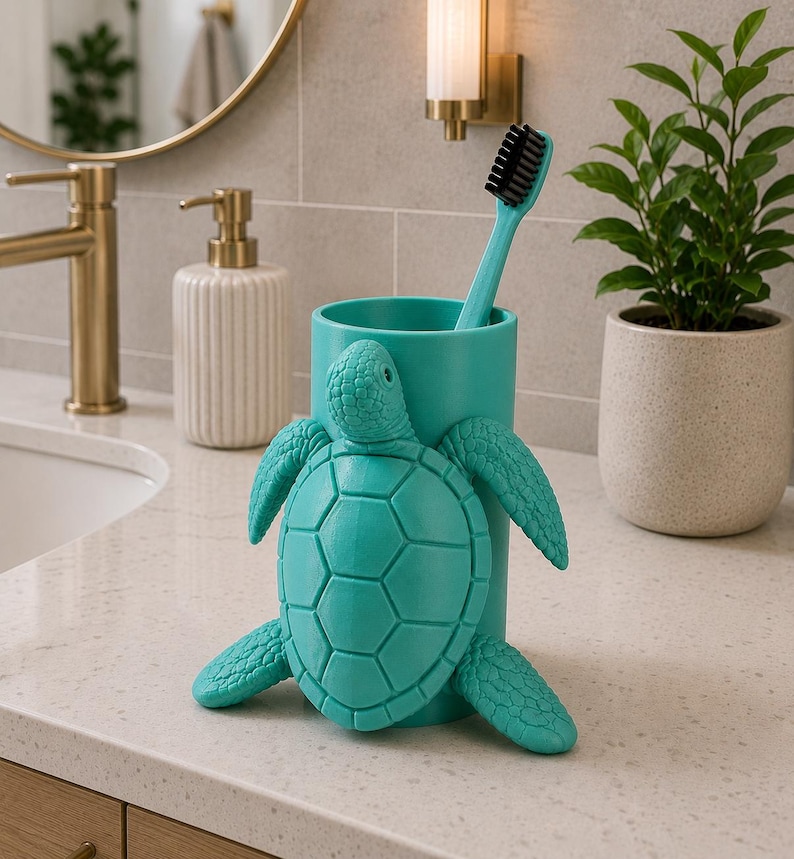 May include: A teal turtle-shaped toothbrush holder with a matching teal toothbrush. The holder is made of a solid material and has a detailed turtle design. The toothbrush has black bristles.