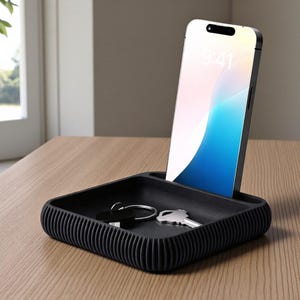 May include: A black, textured tray with a phone and keys. The phone is upright, displaying a blue and white screen. The tray has a ribbed design and sits on a wooden surface. Keys are placed inside the tray.