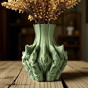 May include: A sage green decorative vase with a unique, textured design, holding dried, golden-brown flowers. The vase has an intricate, sculpted pattern and sits on a wooden surface, creating a natural aesthetic.