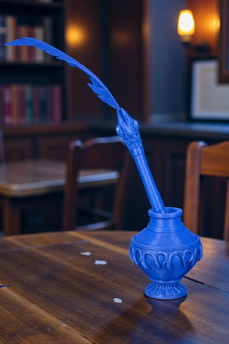 May include: A blue inkwell with a decorative feather pen. The inkwell has a detailed, ornate design and a round base. The feather pen is long and curved, with a detailed head. The inkwell and pen are made of a solid blue material.