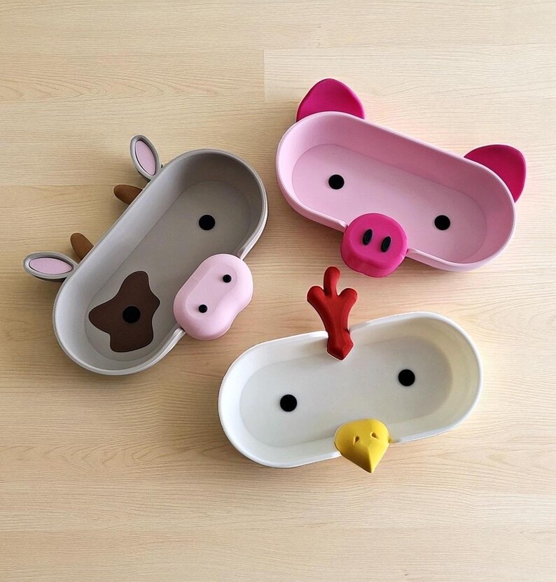 May include: Three animal-themed serving trays: a cow, a pig, and a chicken. The cow tray is gray with brown and pink accents. The pig tray is pink with dark pink ears and snout. The chicken tray is white with red and yellow accents.