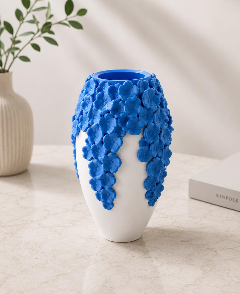 May include: A white ceramic vase with a blue interior and a cascade of blue floral embellishments. The vase has a smooth, glossy finish and a unique, textured design. The vase is a decorative home decor item.
