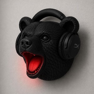 May include: A black bear head sculpture with a textured finish, wearing black headphones. The bear's mouth is open, revealing a red interior. The headphones have the HyperX logo.