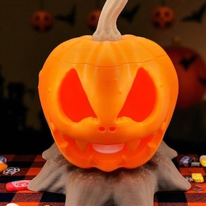May include: An orange, carved pumpkin with a smiling face, lit from within, sits atop a brown, textured base. The pumpkin has triangular eyes and a toothy grin, perfect for Halloween decorations.