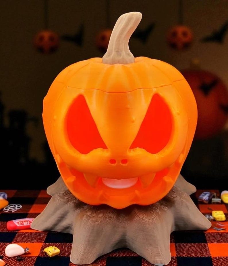 May include: An orange, carved pumpkin with a smiling face, lit from within, sits atop a brown, textured base. The pumpkin has triangular eyes and a toothy grin, perfect for Halloween decorations.