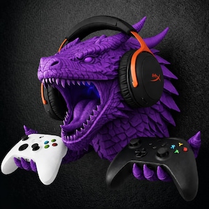 May include: A purple dragon head wall mount featuring textured scales and an open mouth. The dragon wears black and orange over-ear headphones and uses its claws to hold a white game controller on the left and a black game controller on the right.