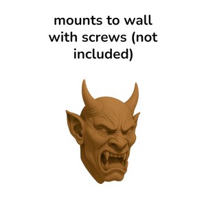 May include: A brown, detailed sculpture of a devil's head with horns, pointed ears, and a snarling expression. The text above reads "mounts to wall with screws (not included)".