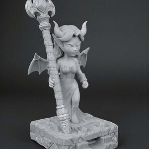 May include: A gray figurine of a female demon with horns, wings, and a staff. The figure stands on a stone base. The staff has a decorative top. The figurine is a fantasy-themed item.