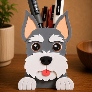 May include: A gray and white dog-shaped desk organizer holding several black, brown, and white pens. The organizer has a cute design with large eyes, a black nose, and a red tongue. The ears are a light orange color. The organizer is sitting on a wooden surface.