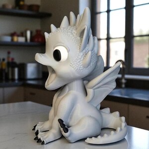 May include: A white dragon figurine with large eyes and an open mouth. The dragon has detailed scales, wings, and black claws. It is sitting on a white surface, with a kitchen in the background.