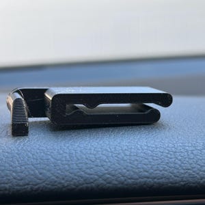 May include: A black plastic clip with a small, textured knob on one end. The clip is designed to hold objects in place.