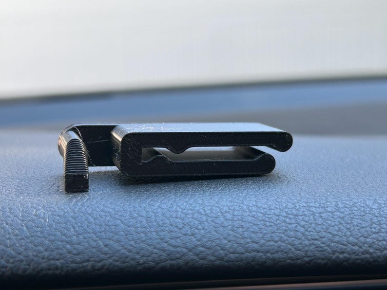 May include: A black plastic clip with a small, textured knob on one end. The clip is designed to hold objects in place.