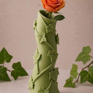 May include: A green vase with a swirling design and ivy leaf accents, holding a vibrant orange rose. The vase is a unique decorative piece, perfect for displaying flowers. The vase is approximately 10 inches tall.