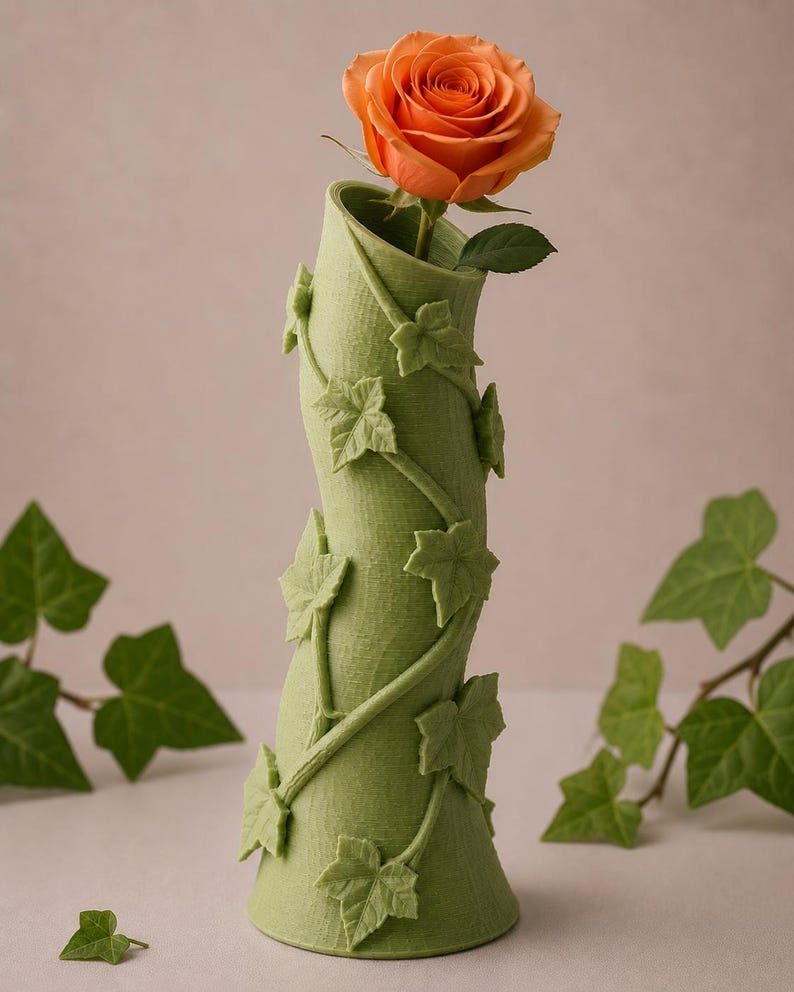 May include: A green vase with a swirling design and ivy leaf accents, holding a vibrant orange rose. The vase is a unique decorative piece, perfect for displaying flowers. The vase is approximately 10 inches tall.