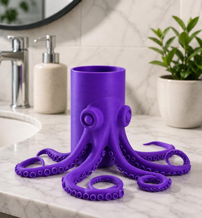 May include: A vibrant purple octopus-shaped toothbrush holder. The holder features a cylindrical body with an octopus design, including tentacles and eye details. The holder is made of a solid, smooth material and is designed to sit on a bathroom counter.
