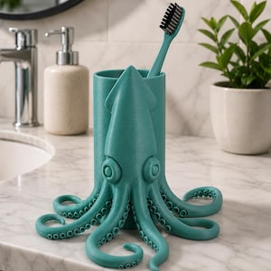 May include: Teal octopus-shaped toothbrush holder with a matching teal toothbrush. The holder has a cylindrical body with an octopus design, including tentacles and large eyes. The toothbrush has black bristles. The holder is on a marble countertop.