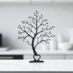 May include: A black metal tree-shaped jewelry holder with a heart-shaped base. The tree has many branches with small leaves, perfect for displaying necklaces, bracelets, and earrings. The jewelry holder is a decorative and functional item.