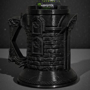 May include: A black, 3D-printed mug shaped like a castle tower, with a handle and decorative details. A green and black Monster Energy drink can sits inside the tower. The mug has a textured brick pattern.