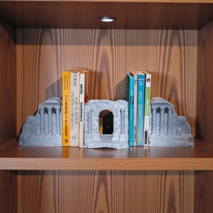 May include: Gray stone bookends shaped like classical ruins, holding a collection of books with colorful spines. The bookends feature columns and architectural details, adding a touch of elegance to the bookshelf.