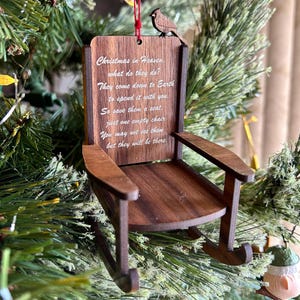 May include: A wooden rocking chair ornament with a red cardinal perched on top. The ornament has a white inscription that reads "Christmas in Heaven. what do they do? They come down to Earth to spend it with you. So save them a seat. just one empty chair. You may not see them but they will be there."