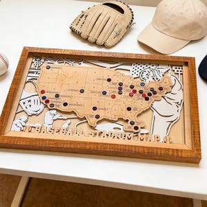 May include: A wooden baseball stadium map of the United States with pins marking locations. The map is in a brown wooden frame, with a baseball, glove, and cap nearby. The text "BASEBALL STADIUM MAP" is visible.